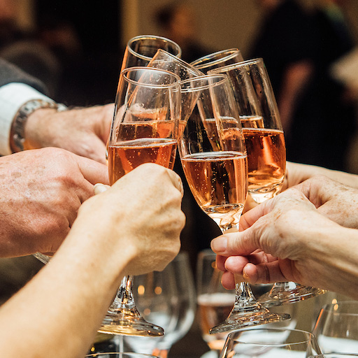 Wine flutes filled with rose cheers-ing. Tight crop of hands and glasses.